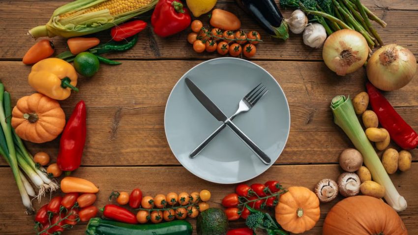 Top view of fresh vegetables creatively arranged around an empty plate on a wooden table.